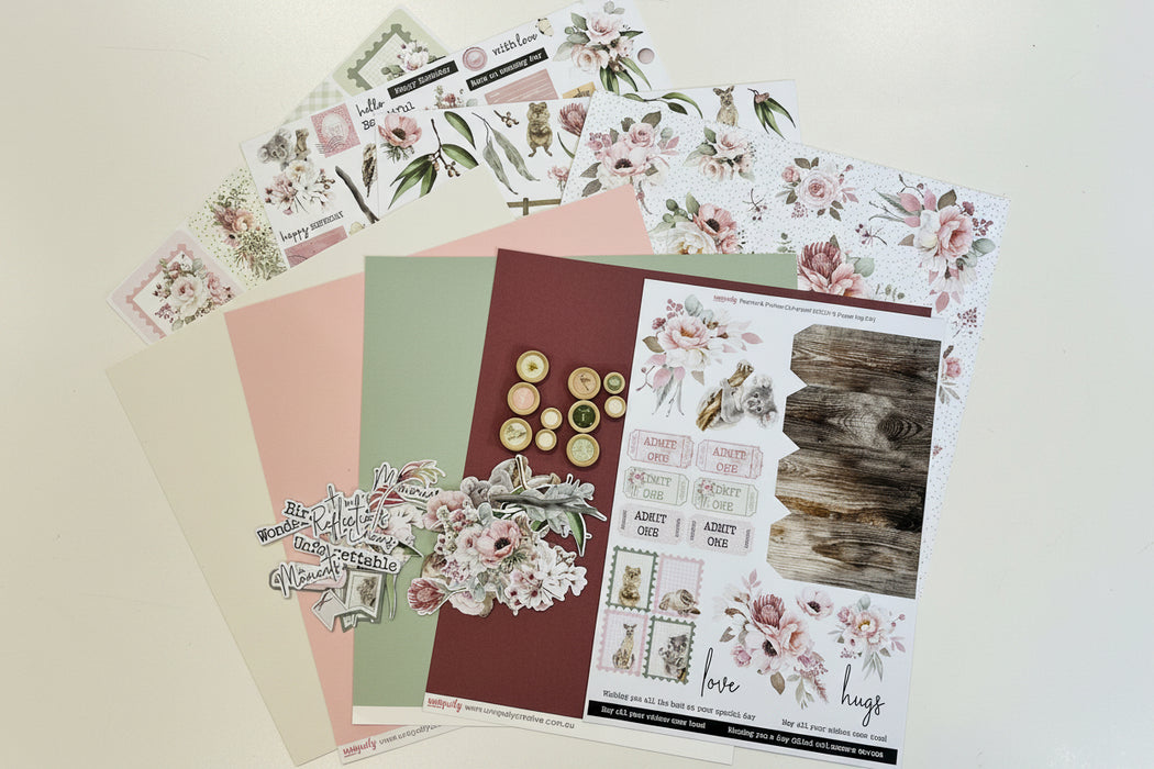 A flat lay of floral scrapbooking paper sheets and sticker sheets arranged on a pale yellow background. The sheets feature pink and cream roses, green leaves, vintage-style stamps, buttons, and a rustic wood texture.